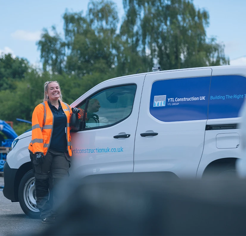 Employee in PPE stood smiling next to a YTL Construction van